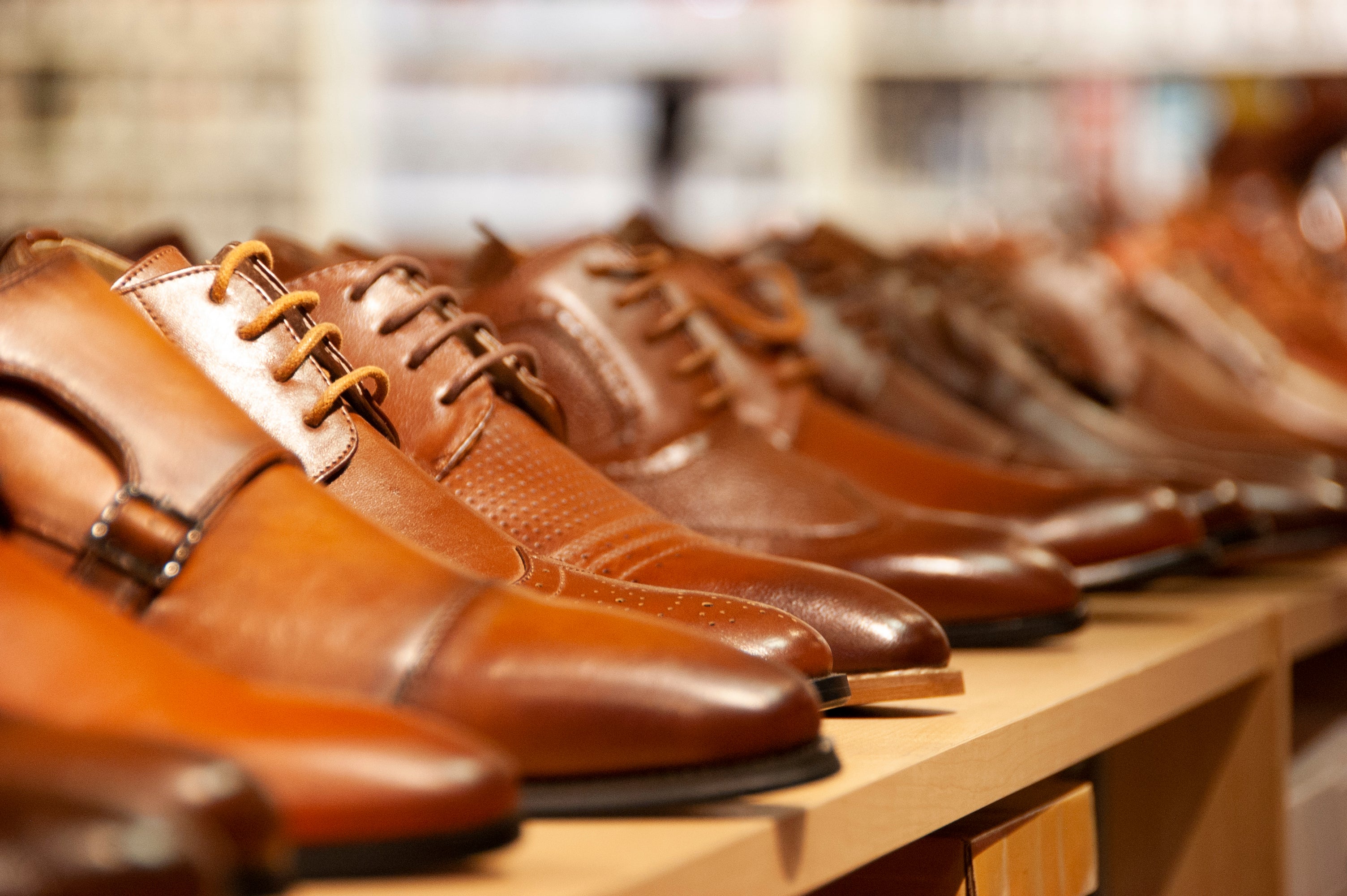 A close-up view of a row of polished brown leather men's dress shoes lined up neatly on a wooden display shelf.
